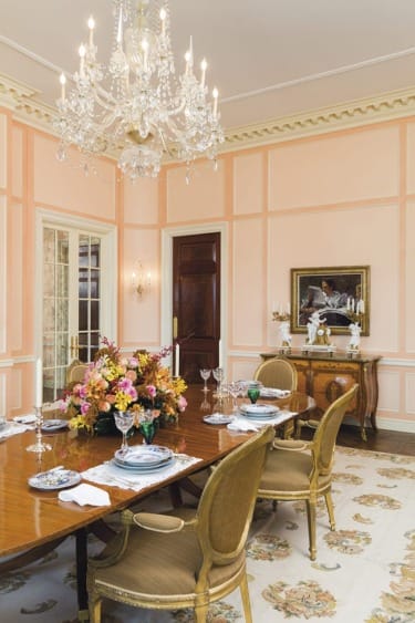 Elegant dining room with a wooden table, floral centerpiece, chandelier, classic chairs, and ornate wall paneling.