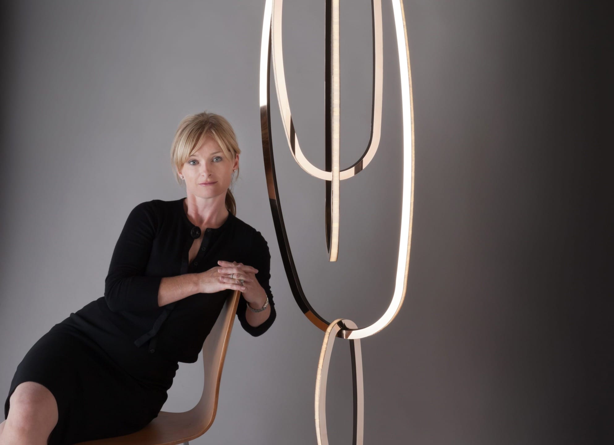Woman in black dress sitting next to modern sculpture against gray background