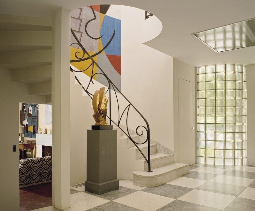 Art Deco staircase with curved railing, geometric wall design, sculpture on pedestal, and checkered floor tiles.