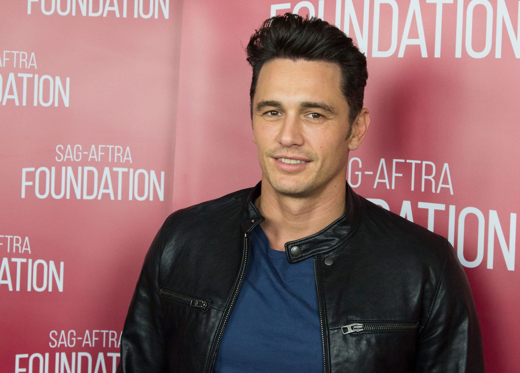 Person in a leather jacket standing in front of a red SAG-AFTRA Foundation backdrop.