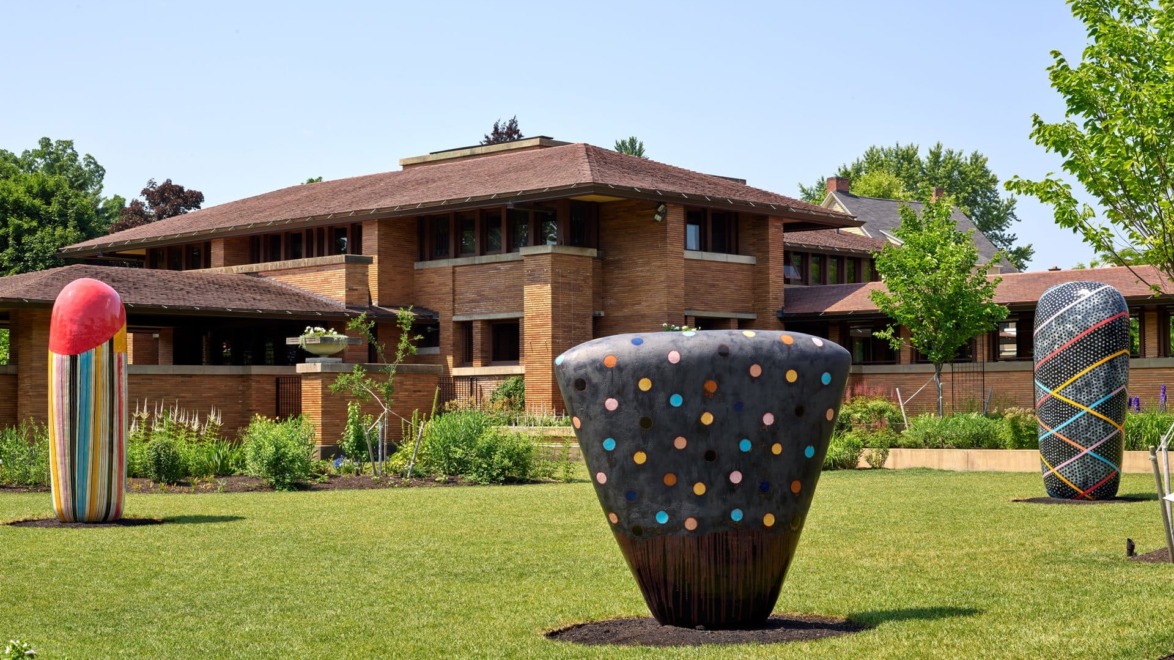 Historic brick building with unique sculptures on the lawn, featuring colorful patterns and shapes under a clear blue sky.