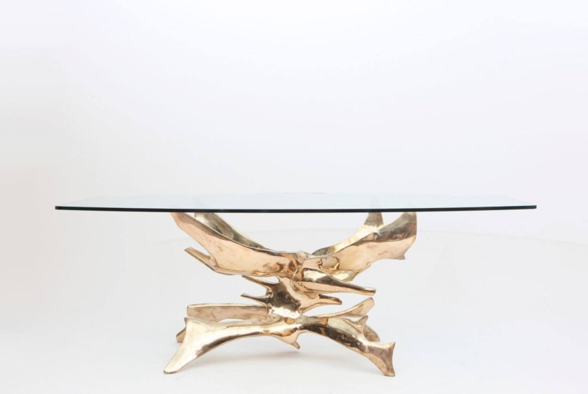 Elegant glass-top dining table with a unique gold sculptural base against a plain white background.