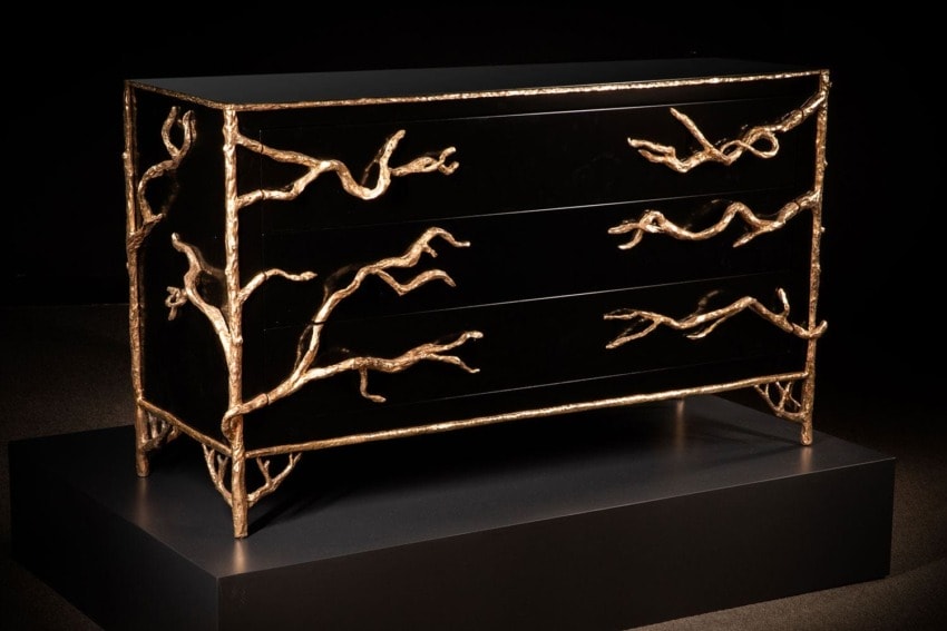 Elegant black dresser with intricate gold branch-like details displayed in a dimly lit setting.