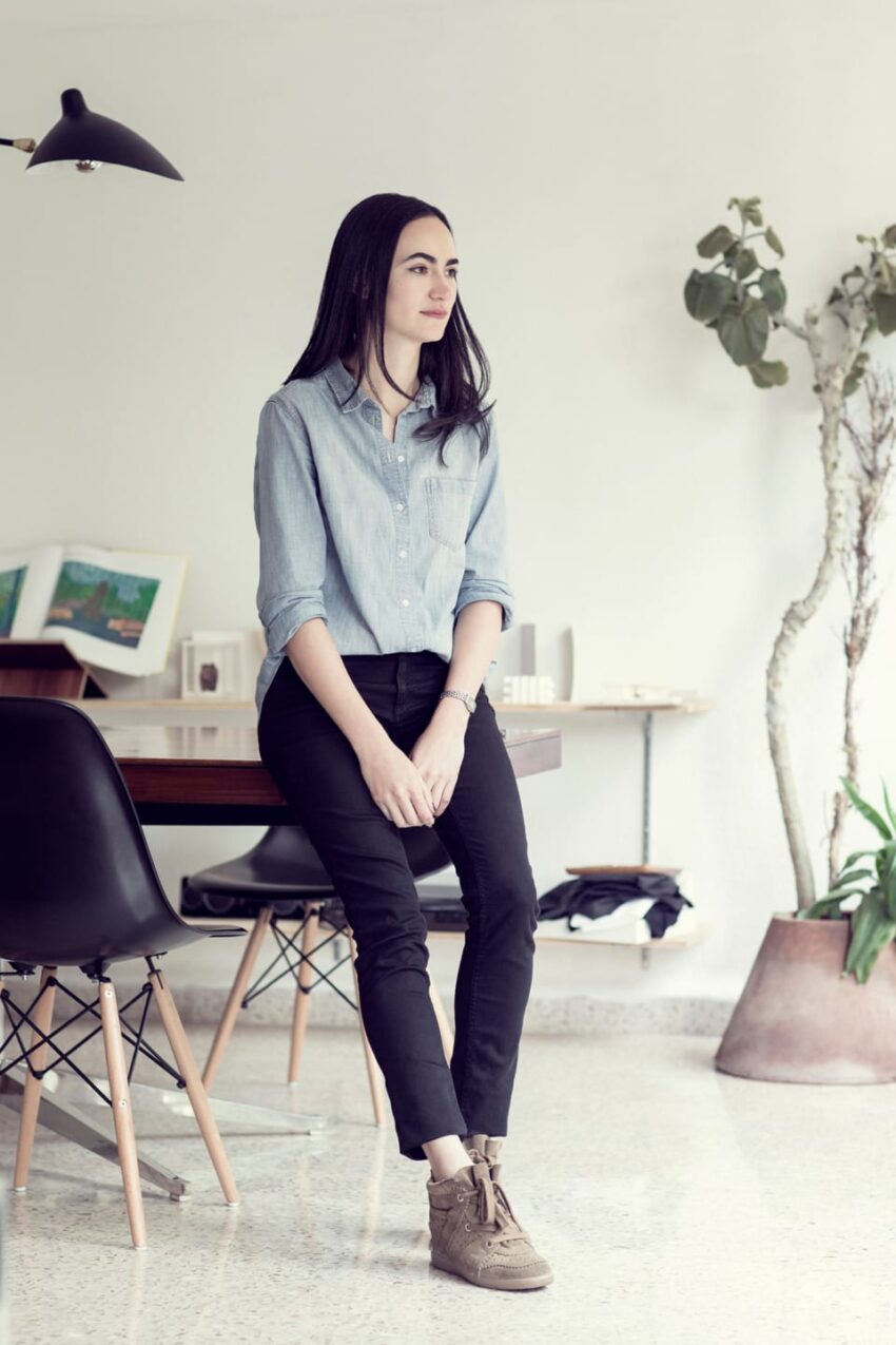 Woman sitting on a table in a modern office with plants and art in the background