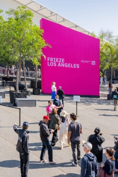 Visitors gathering outside Frieze Los Angeles art fair entrance with bright pink signage and sunny weather.
