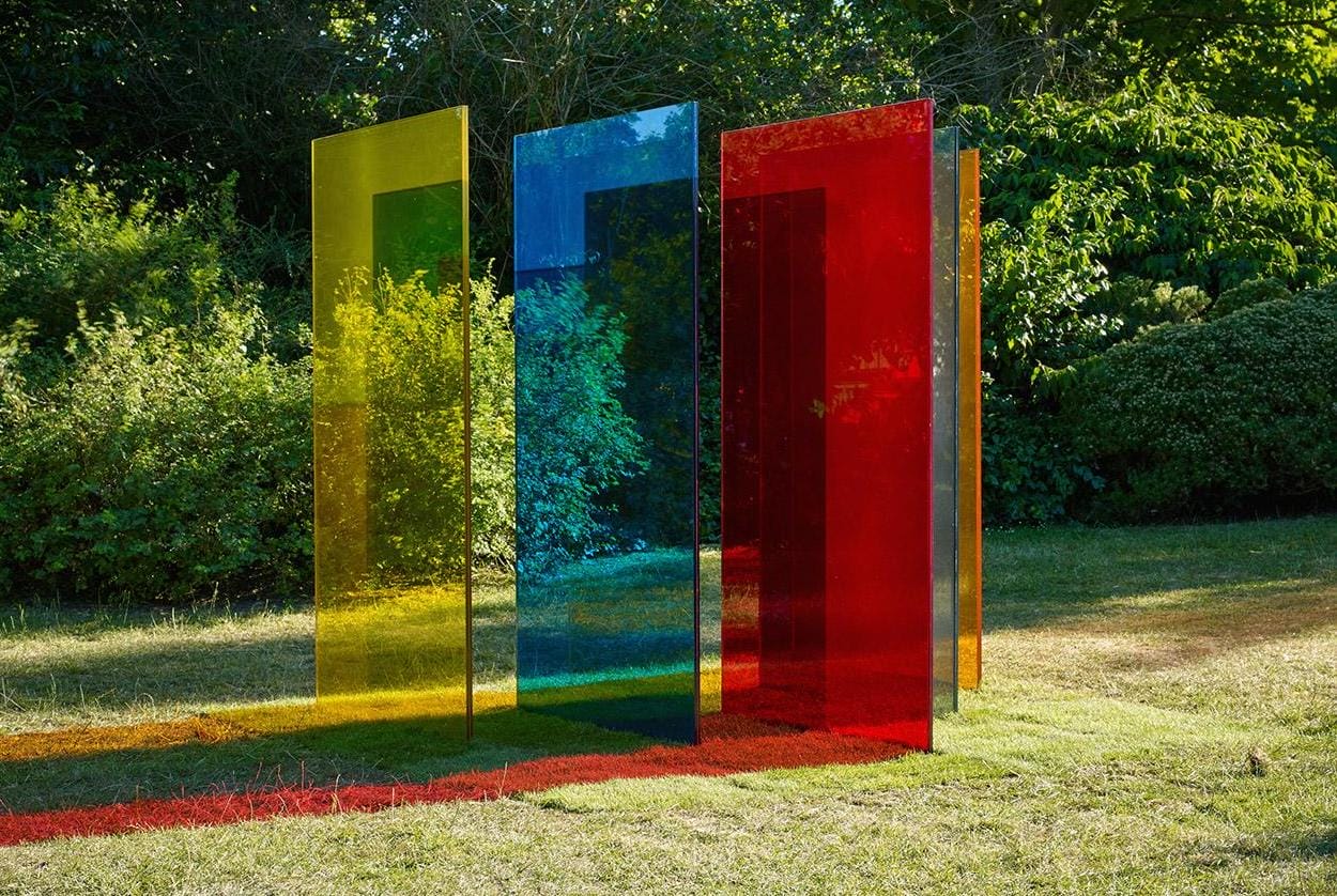 Colorful transparent glass panels standing on grass in a sunny garden.
