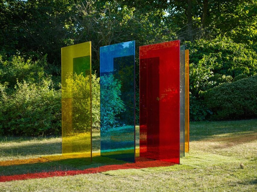 Colorful transparent panels standing on grass in a park setting with trees in the background.