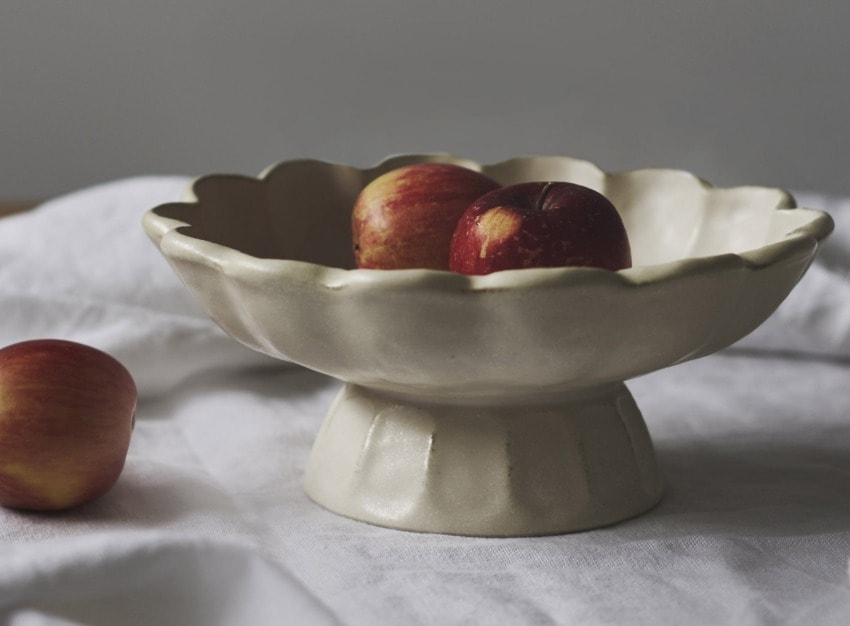 Ceramic fruit bowl with apples on a white cloth background, one apple outside the bowl.