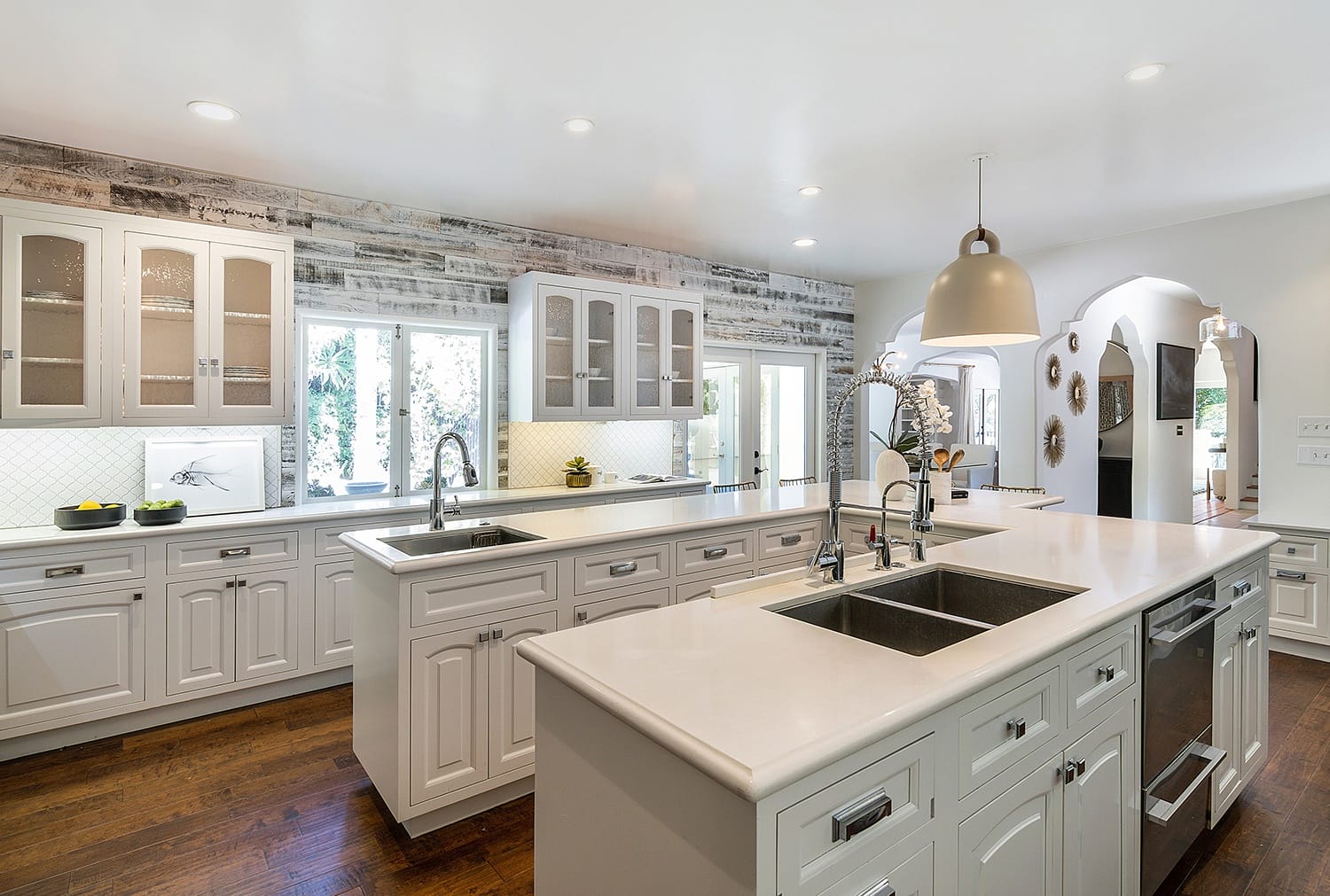 Spacious modern kitchen with white cabinets, dual sinks, and pendant lighting on hardwood floors.
