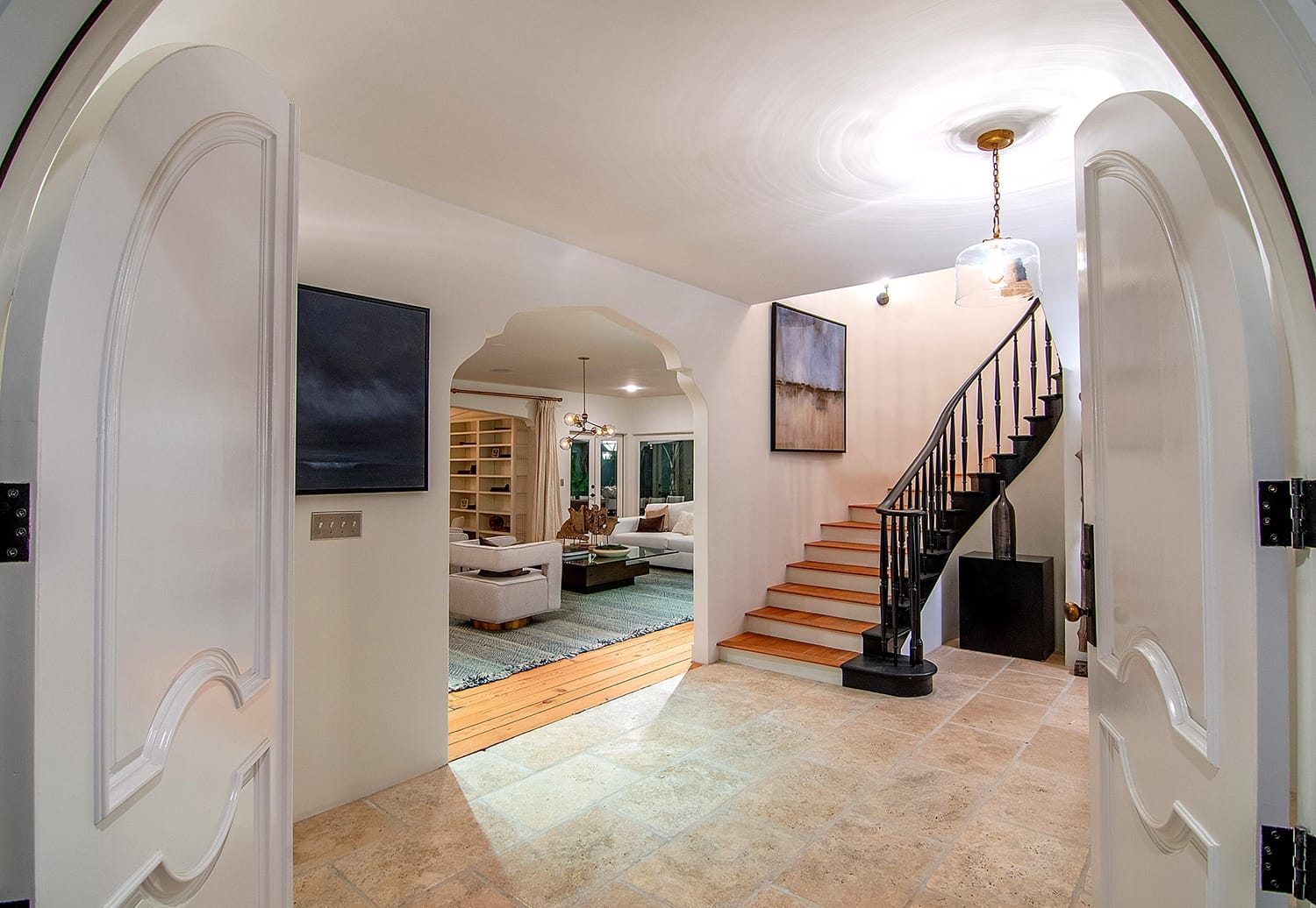 Spacious home entryway with open double doors, stone flooring, and a staircase leading to an inviting living area.