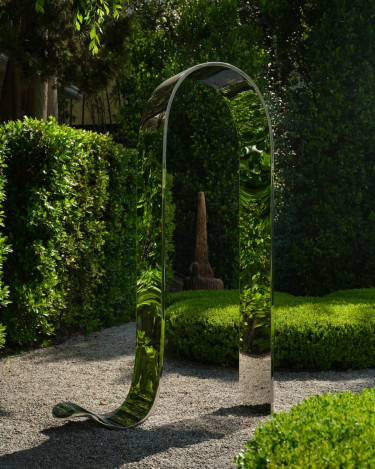 Modern metallic sculpture in a lush green garden with gravel path