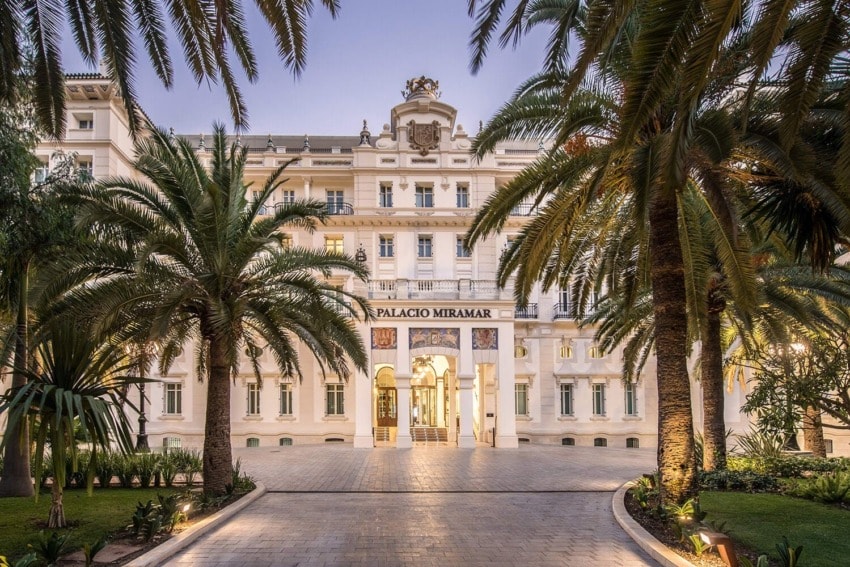 Grand hotel entrance surrounded by tall palm trees with intricate architectural details and illuminated facade.