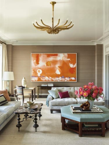 Elegant living room with modern art, neutral sofas, vibrant flowers on coffee table, and a gold chandelier.