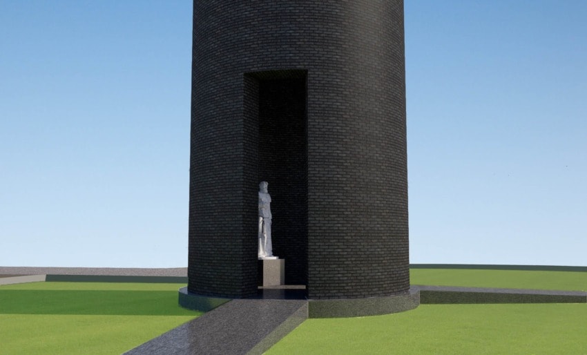 Brick tower with a statue in a recessed alcove, surrounded by green grass and a clear blue sky in the background.