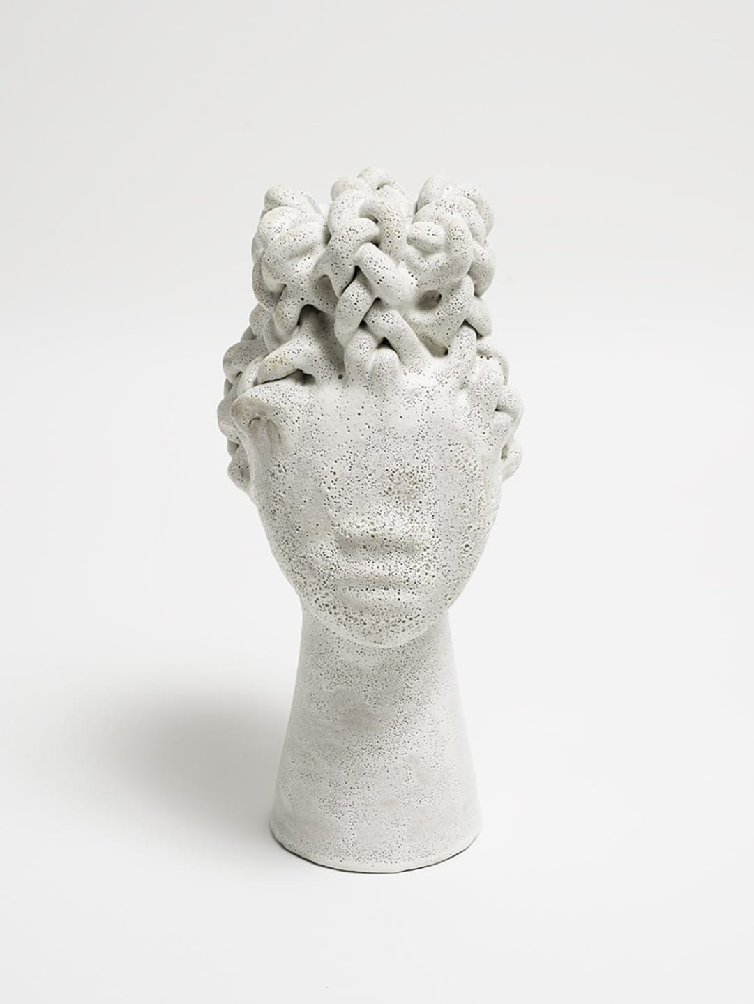 White stone sculpture of a person's head with intricately braided hairstyle displayed against a plain background.