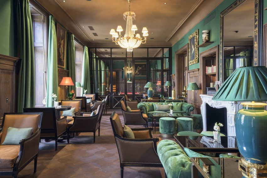 Elegant hotel lounge with green walls, plush seating, chandeliers, and a cozy fireplace, exuding a vintage yet luxurious ambiance.