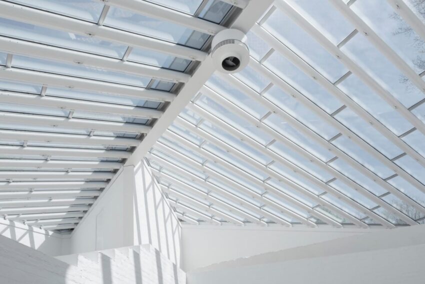 Modern glass ceiling with metal beams and a security camera in a bright, sunlit interior space.