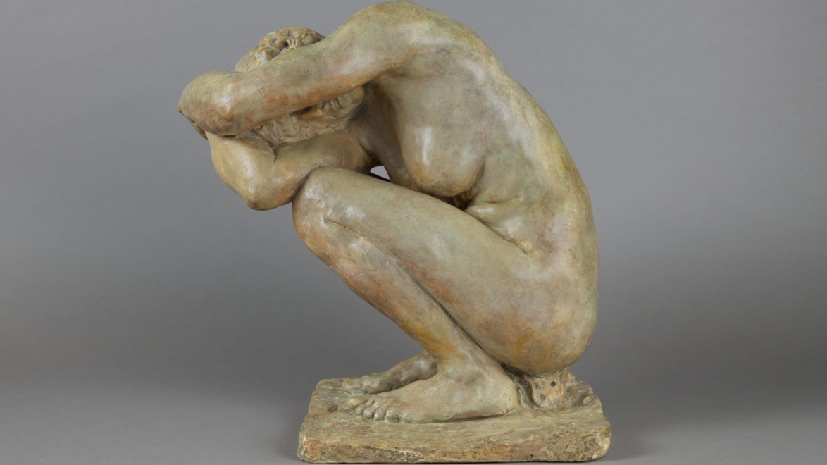 Bronze sculpture of a crouching person with arms folded over head on a rectangular base against a gray background.