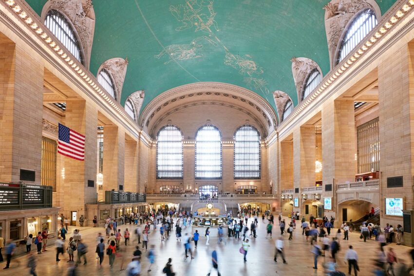 Grand Central Terminal's bustling interior with a celestial ceiling, crowds of people, and the American flag visible.