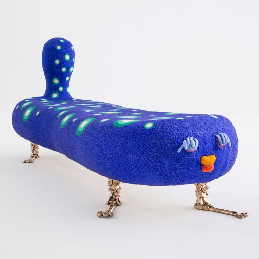 Colorful, abstract bench with a blue and green design, featuring playful eyes and lips, and gold quirky legs.