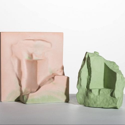 Two abstract ceramic sculptures, one pink with smooth curves and one green with jagged edges, on a plain background.