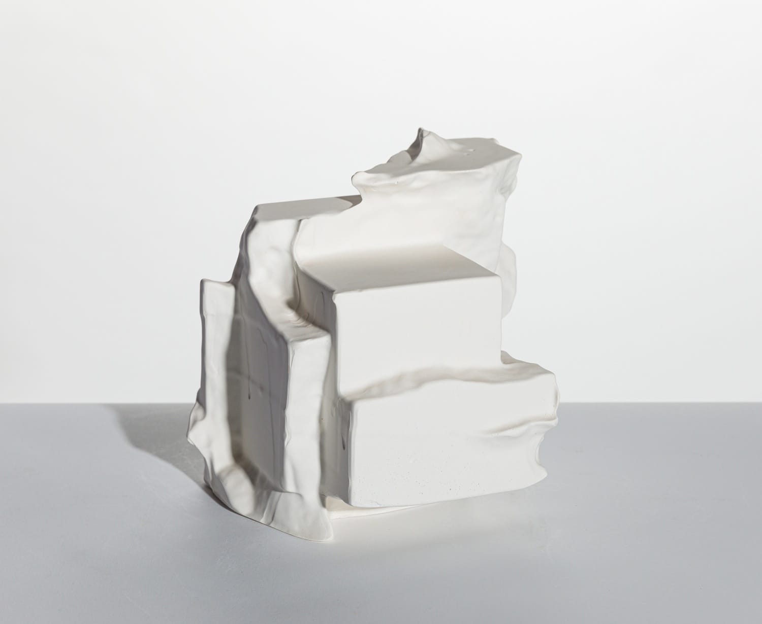 Abstract white ceramic sculpture with layered geometric forms on a plain background.