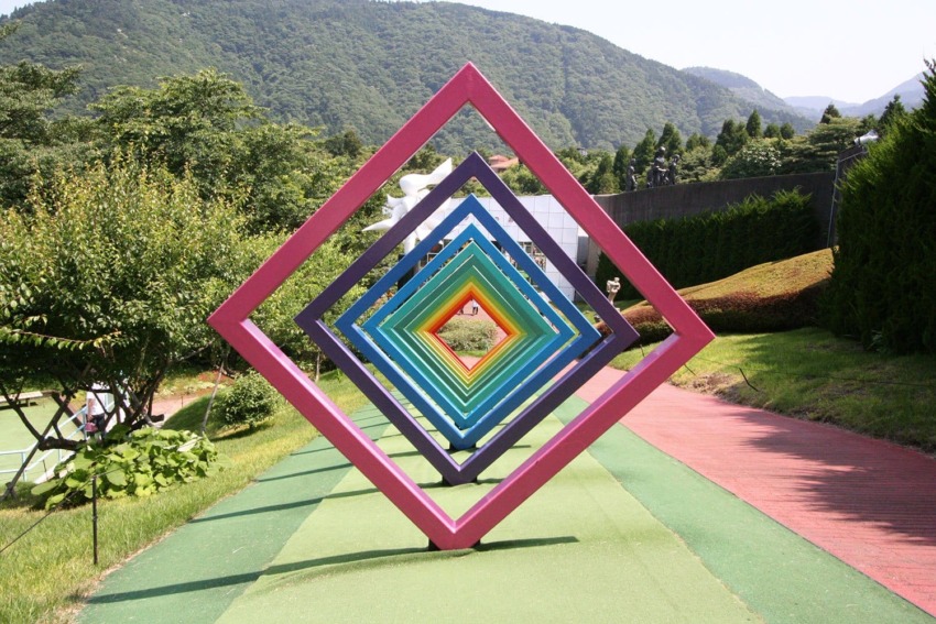 Colorful geometric diamond-shaped frames arranged in a row outdoors with mountains and greenery in the background