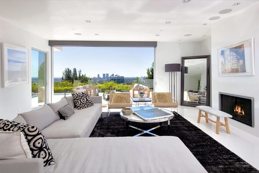Modern living room with white sofa, fireplace, and cityscape view through large window. Bright and spacious interior.