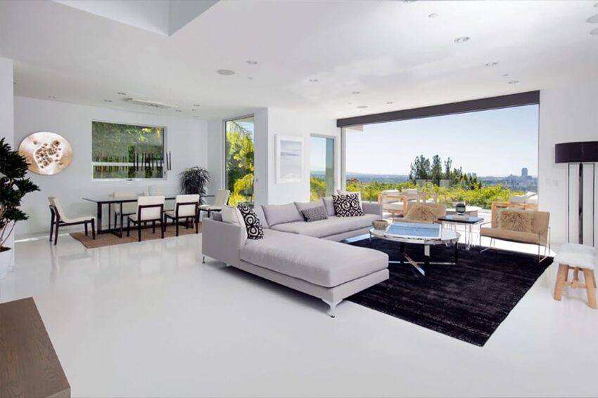 Modern living room with white furniture, large windows, and a scenic view outside, featuring a spacious dining area.