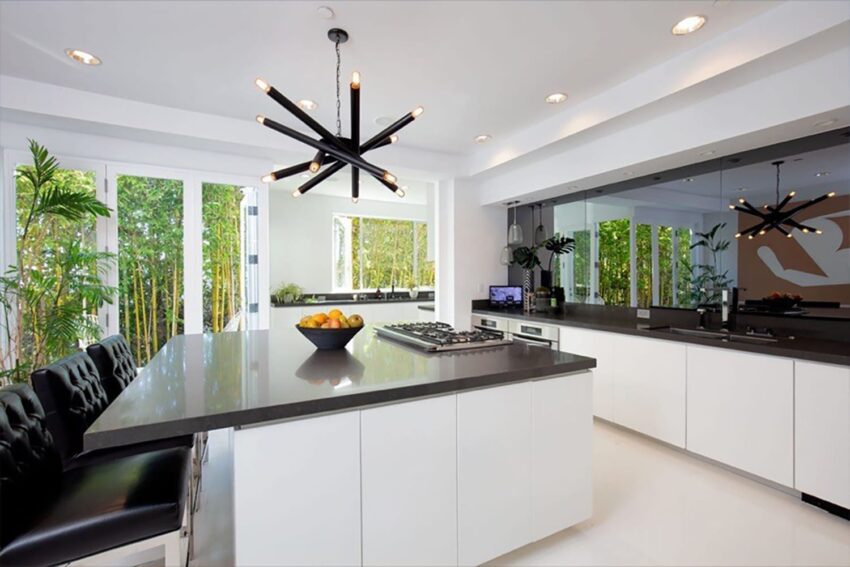 Modern kitchen with sleek white cabinets, large island with dark countertop, and contemporary light fixture above.
