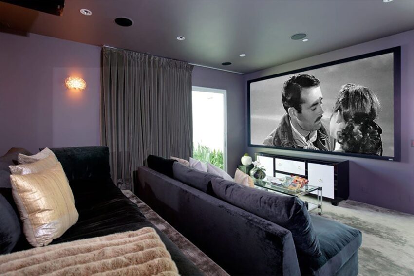 Home theater room with velvet sofas, pillows, and a large screen displaying a black and white movie scene.