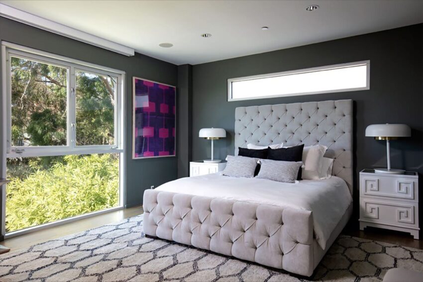 Modern bedroom with tufted bed, patterned rug, and large window with garden view.