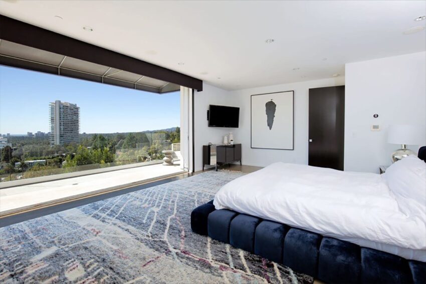 Modern bedroom with large windows, blue carpet, white bed, and cityscape view.