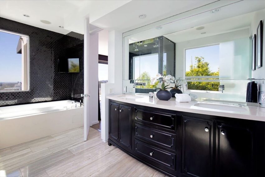 Modern bathroom with black vanity, large mirror, bathtub, and windows with a view of greenery outside.