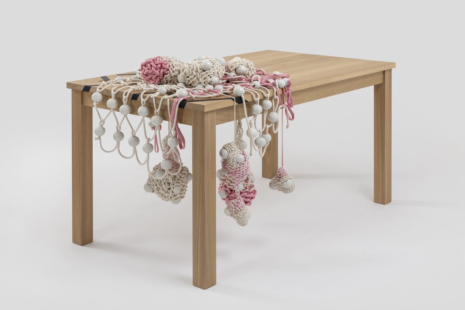 Wooden table decorated with assorted macramé ornaments in pink, white, and beige tones hanging off the edges.