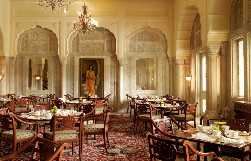 Elegant dining room with ornate chandeliers, plush seating, and set tables, featuring intricate arches and a traditional interior design.