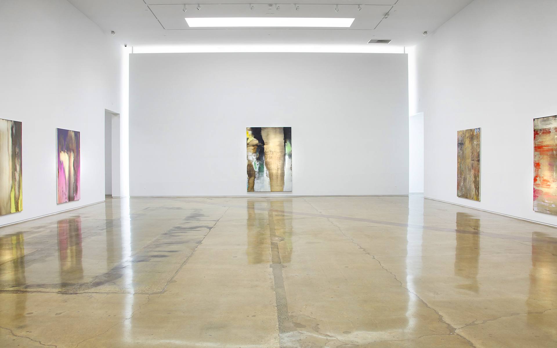 Art gallery interior with polished concrete floors and abstract paintings on white walls.