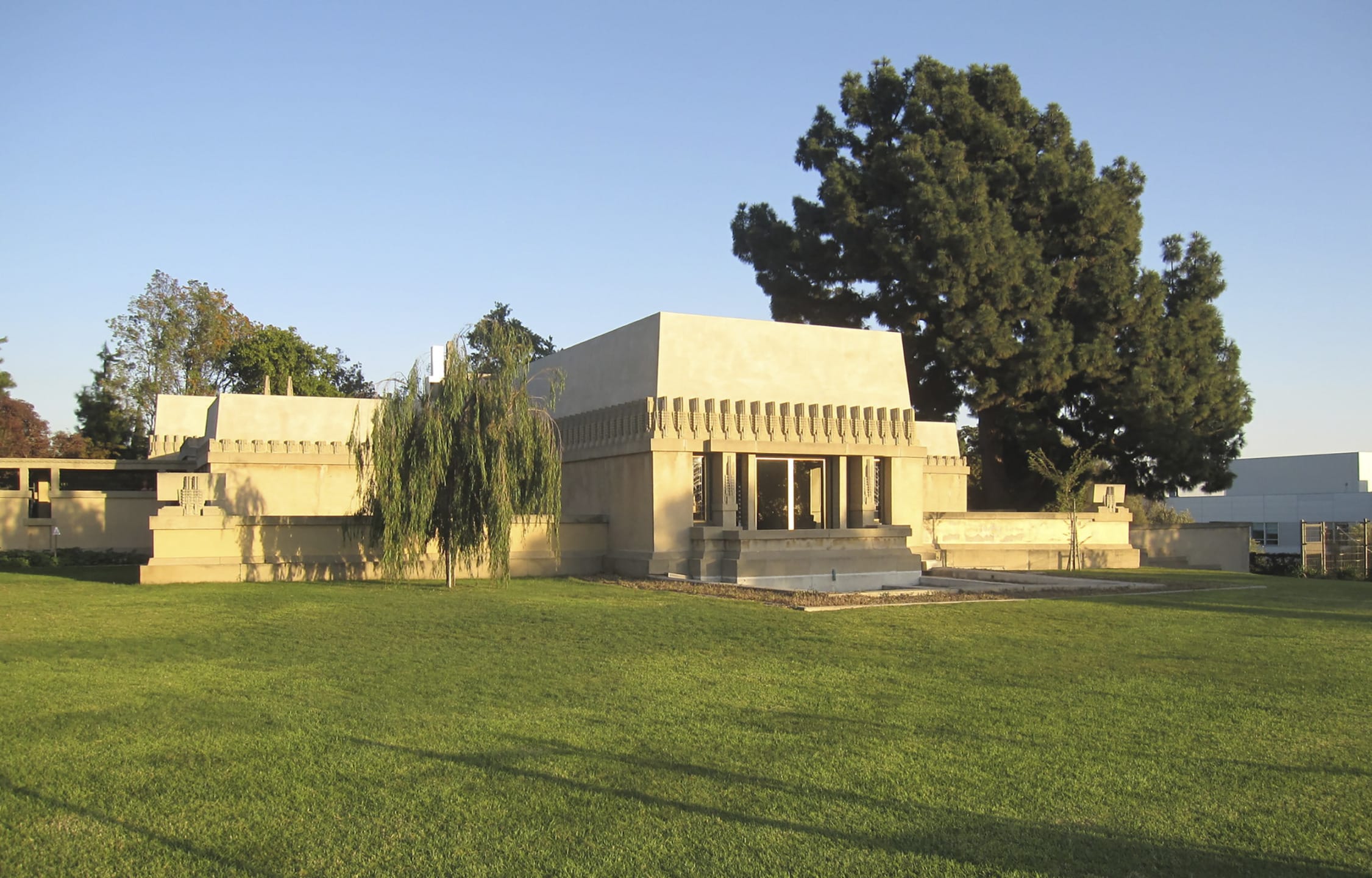 Historic concrete house with unique architecture, surrounded by trees and a large grassy lawn, under a clear blue sky.