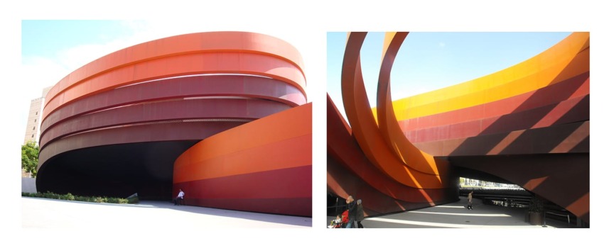 modern architecture with bold red and orange curved exterior, featuring a person walking for scale