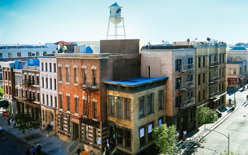 Aerial view of a row of vintage-style building exteriors with a water tower in the background on a clear day.