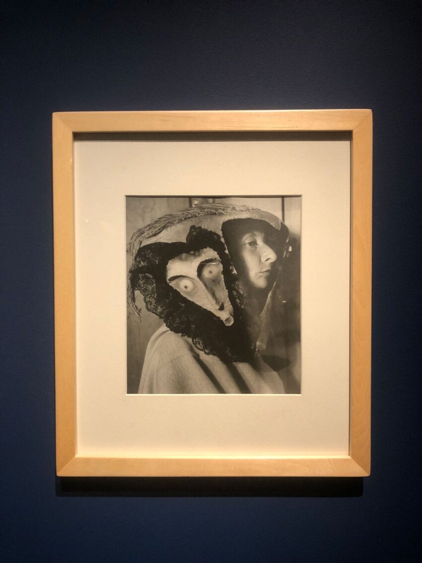 Framed black and white photograph of two people wearing theatrical masks and cloaks, displayed on a dark wall.
