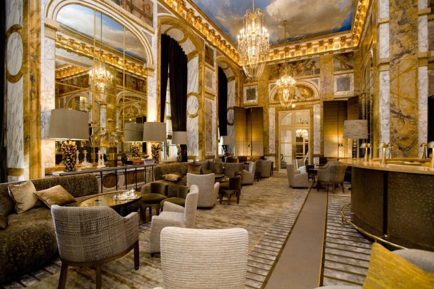 Luxurious hotel lounge with elegant chandeliers, plush seating, marble accents, and ornate ceiling detailing.