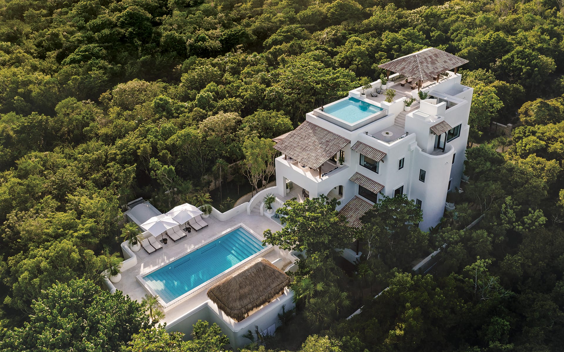 Luxury villa with two pools surrounded by lush greenery in a tropical setting, view from above.