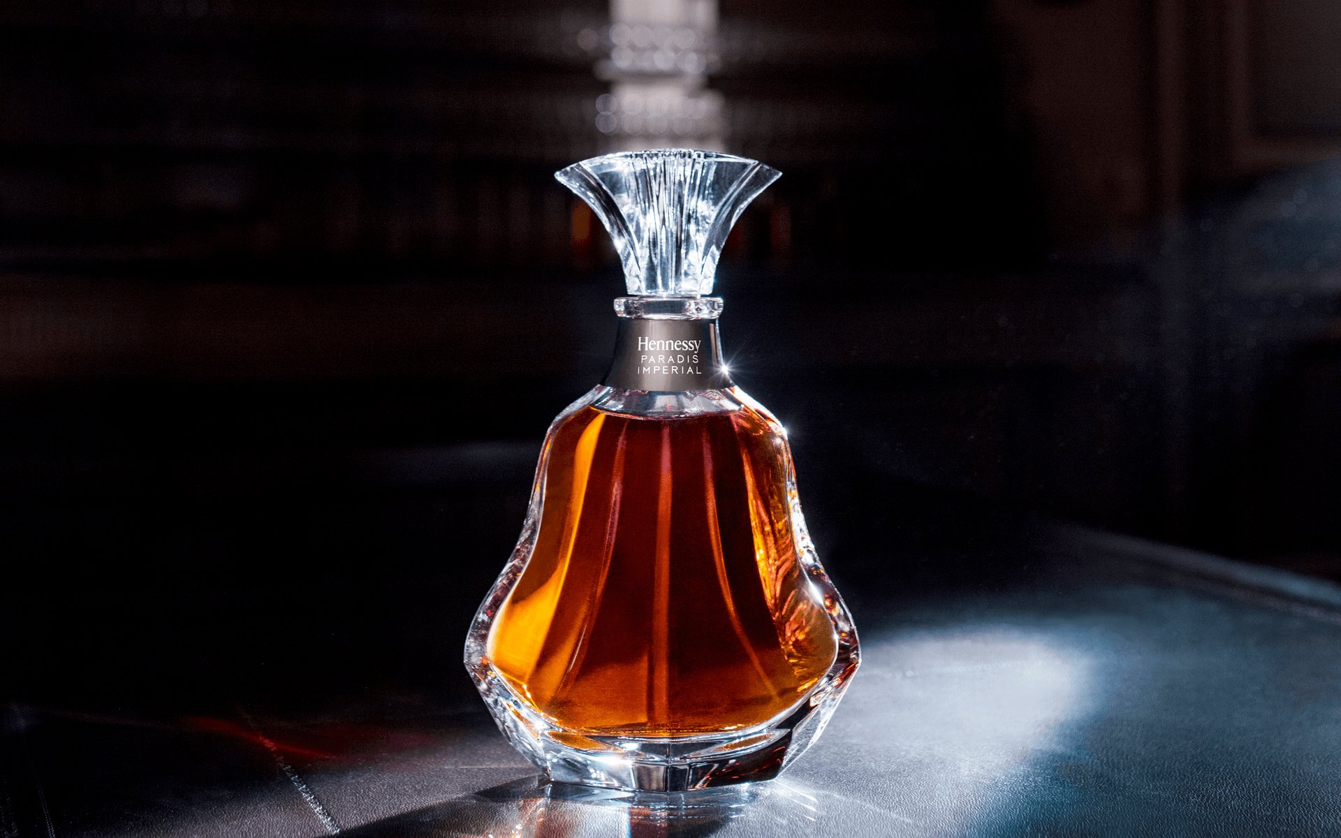 Elegant glass bottle of cognac with amber liquid on a dark reflective surface, illuminated by soft lighting.
