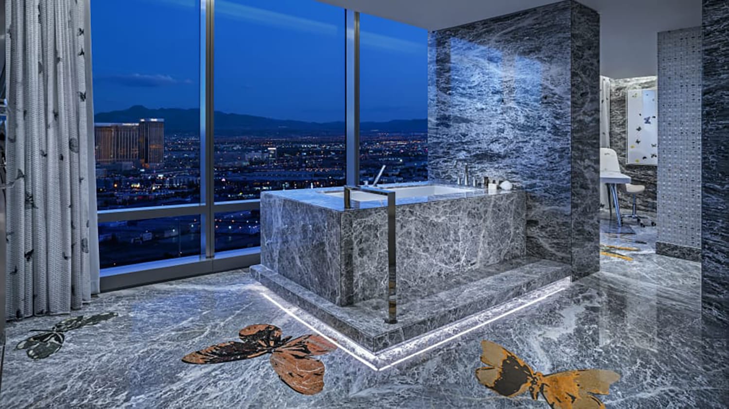 Luxurious marble bathroom with a large tub, large windows with a city view, and butterfly designs on the floor.