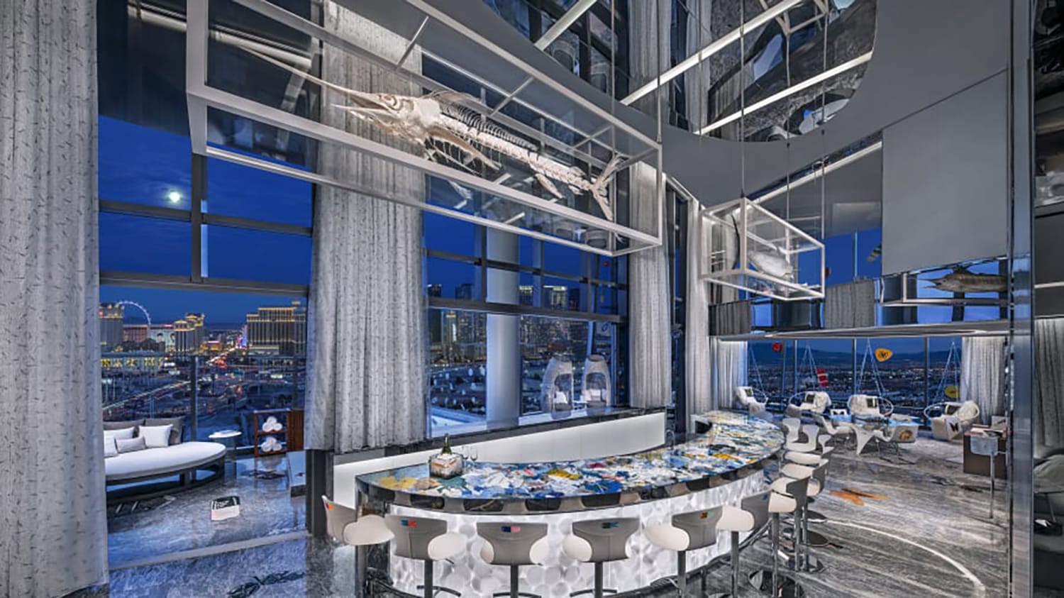 Luxurious modern bar with artistically designed interior, ocean-themed decor, and large windows overlooking a night cityscape.