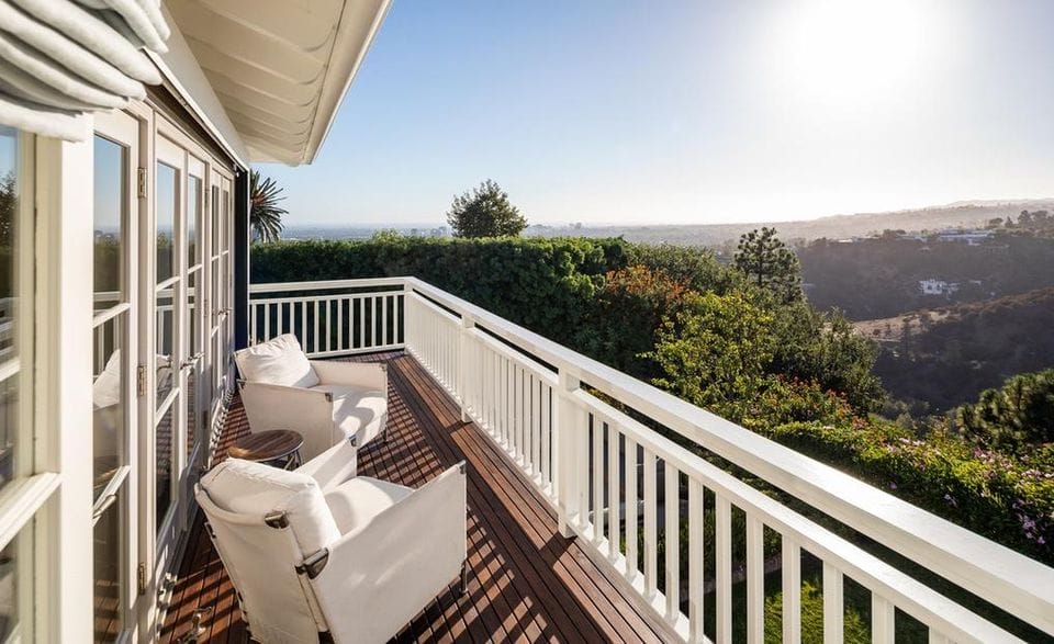 Scenic view from a house balcony with chairs overlooking lush greenery and a distant landscape.