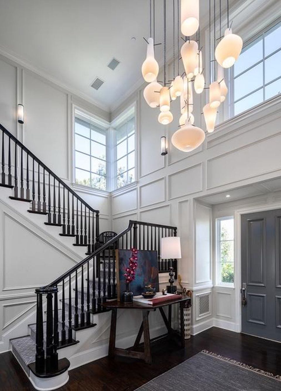 Elegant foyer with dark wooden staircase, modern chandelier, large windows, and contemporary decor.