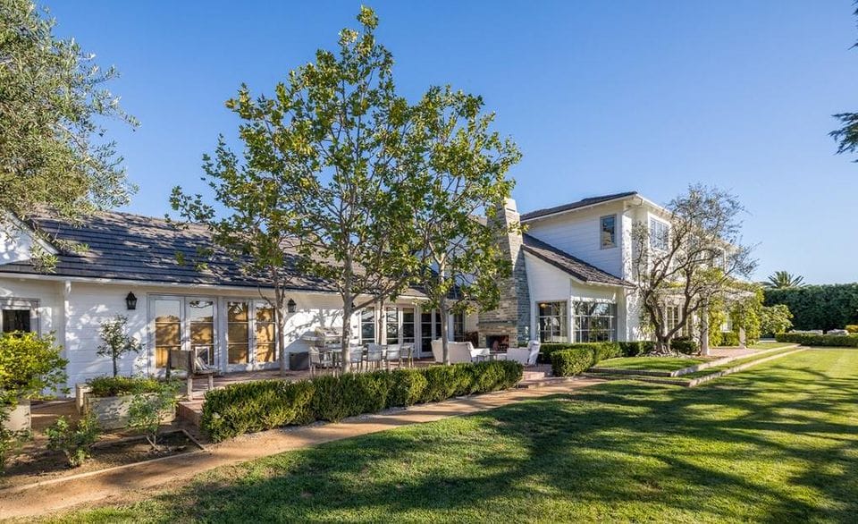 Luxury modern farmhouse with large windows, lush green lawn, and clear blue sky background.