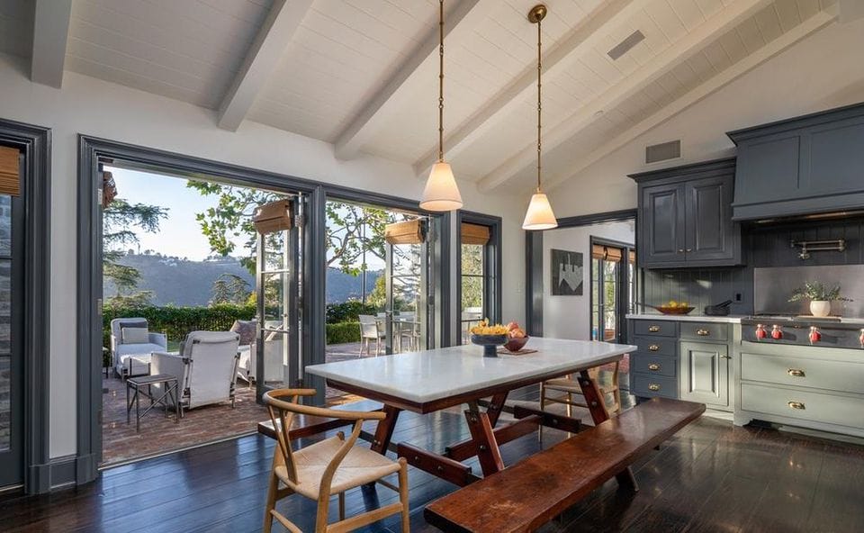 Spacious kitchen with a dark wood dining table, blue cabinets, and large windows opening to a patio with mountain views.